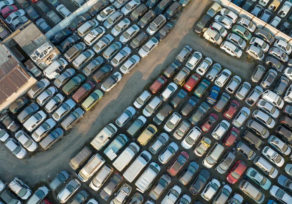 Aerial view of big parking lot of junkyard with rows of discarded broken cars.